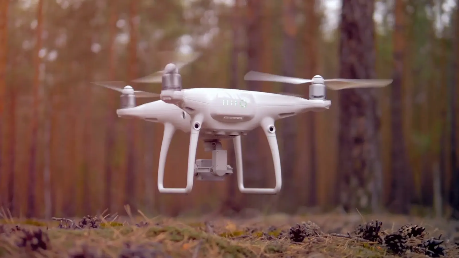 A white camera drone hovers above a forest floor. Still from the YourLegend showreel.