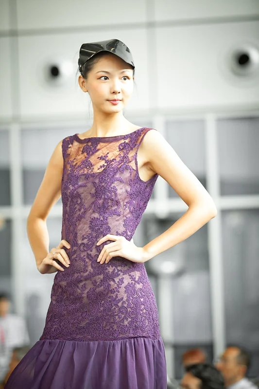 A model in a purple lace dress poses on the runway.