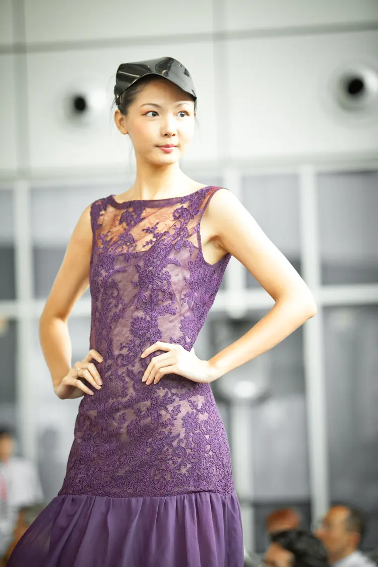 A model in a purple lace dress poses on the runway.